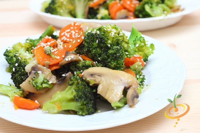 Stir-fried broccoli, carrots, and mushrooms garnished with sesame seeds on a white plate
